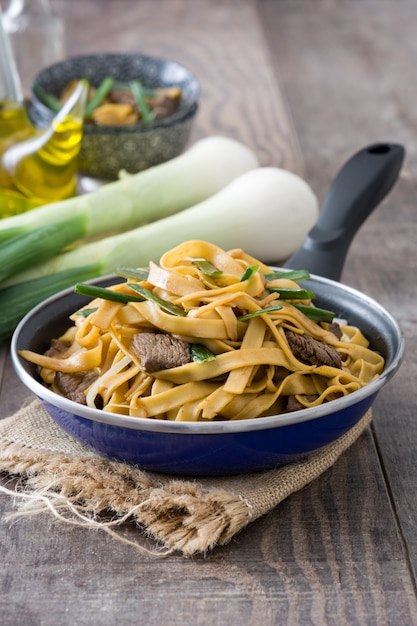 Beef chow mein in a frying pan on wooden table