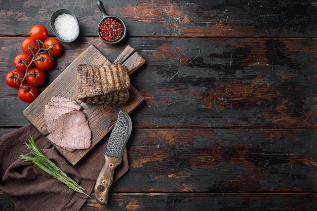 Beef cold meat cut on wooden cutting board on old dark wooden table background top view flat lay with copy space for text