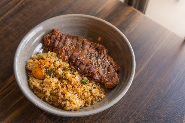 Photo beef fat garlic fried rice with beef steak and topping with pickled egg yolk in a bowl