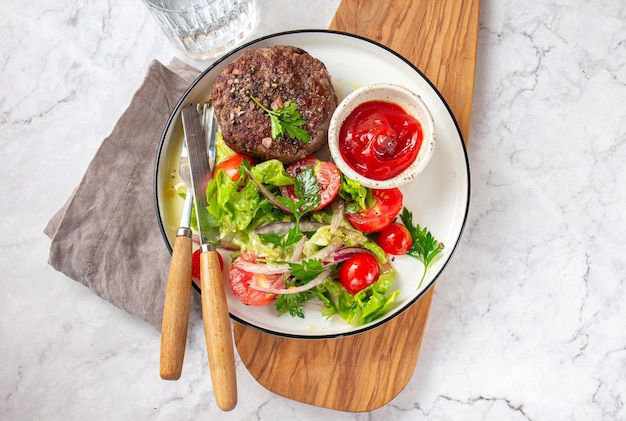 Beef hamburger with lettuce tomato salad on white plate top view