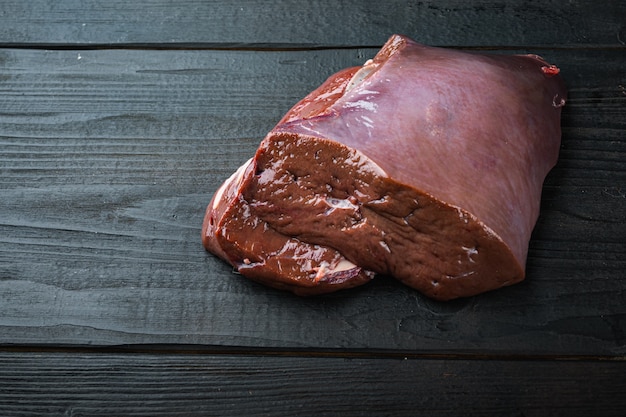 Beef liver on black wooden background with copy space.