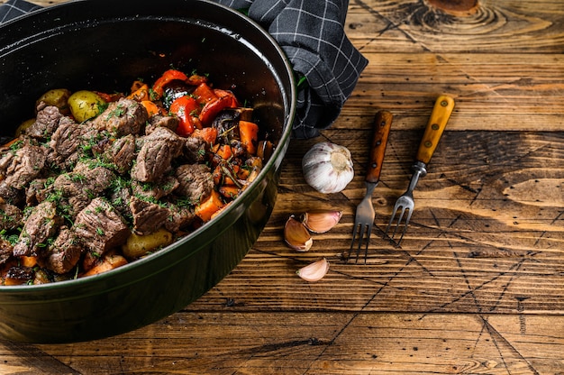 Beef meat stew with potatoes, carrots and herbs. Wooden background. Top view. Copy space.