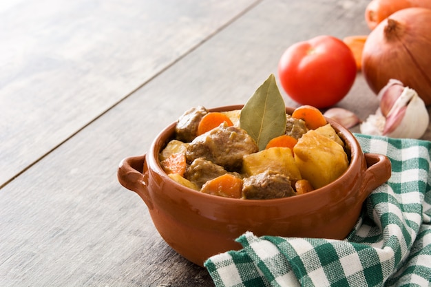 Beef meat stewed with potatoes, carrots and spices in bowl on wooden table copy space