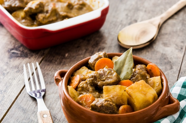 Beef meat stewed with potatoes, carrots and spices in bowl on wooden table