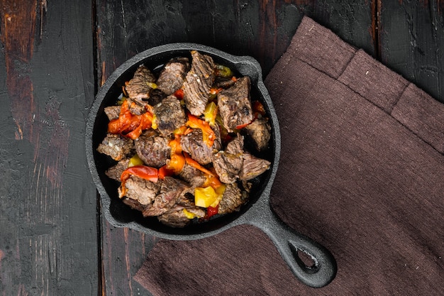 Beef meat stewed with potatoes, carrots and spices set, in cast iron frying pan, on old dark  wooden table, top view flat lay, with copy space for text