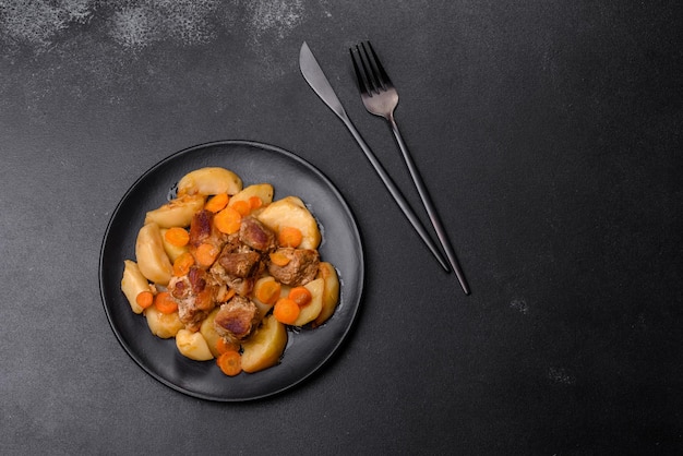 Photo beef meat and vegetables stew on a black plate with roasted potatoes