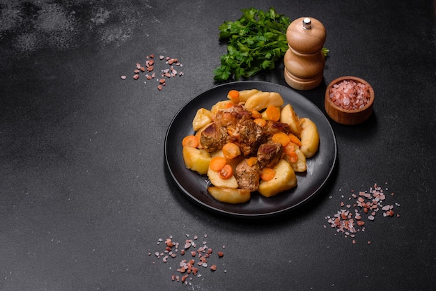 Beef meat and vegetables stew on a black plate with roasted potatoes