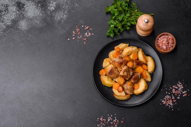 Beef meat and vegetables stew on a black plate with roasted potatoes