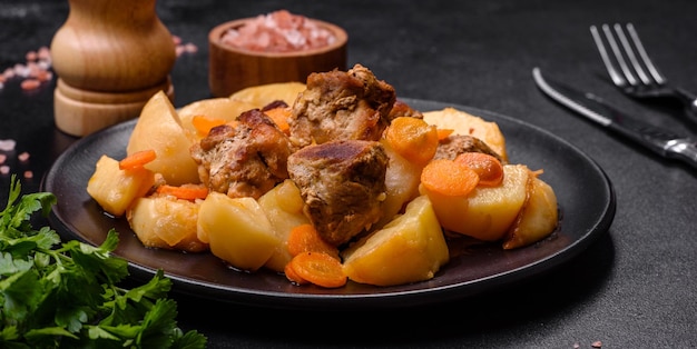 Beef meat and vegetables stew on a black plate with roasted potatoes