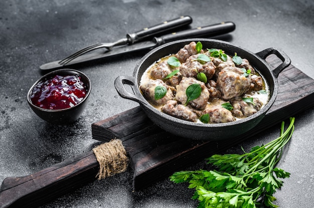 Beef meatballs in cream sauce in a frying pan. Black background. Top view.