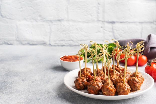 Beef meatballs stewed in tomato sauce on a plate on barbecue skewers