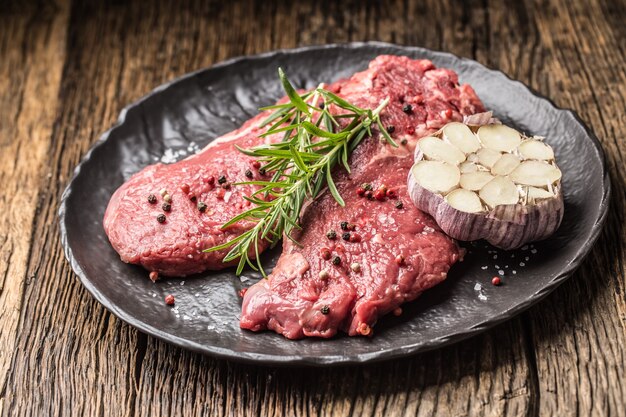 Beef meeat Rib-Eye steak wit rosemary salt and pepper on black plate.