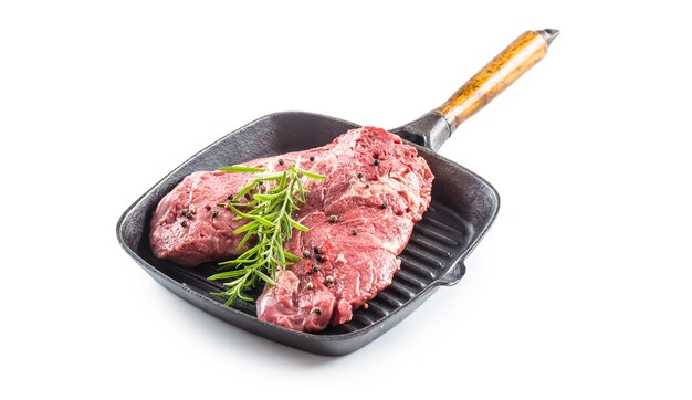 Beef meeat Rib-Eye steak wit rozemarijn zout en peper in grill pan geïsoleerd op wit.