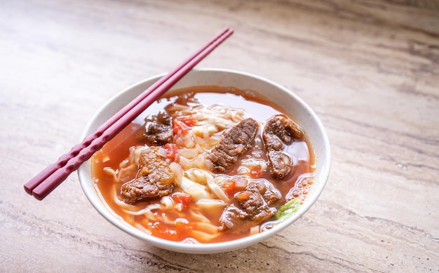 明るい木製のテーブルの上にボウルにトマトソースのスープが入ったビーフヌードルラーメンの食事台湾で有名な中国風の食べ物をクローズアップ上面図コピースペース