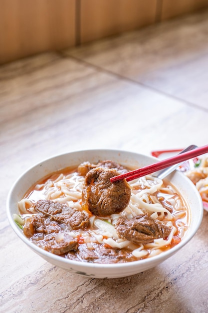 明るい木製のテーブルの上にボウルにトマトソースのスープが入ったビーフヌードル台湾ラーメン料理有名な中華風料理をクローズアップ上面図コピースペース