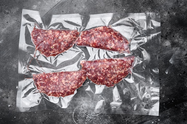 Beef patties in a vacuum packing set, on black dark stone table
background, top view flat lay