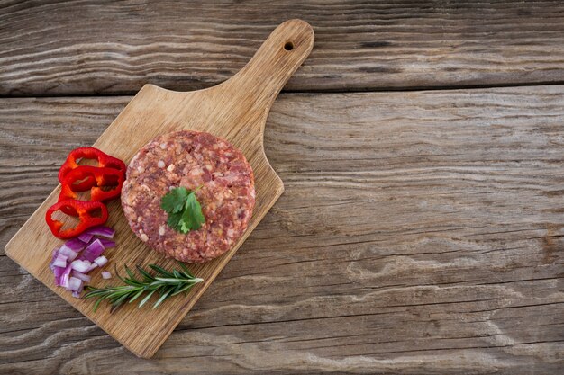 Beef patty and ingredients on wooden tray against wooden surface