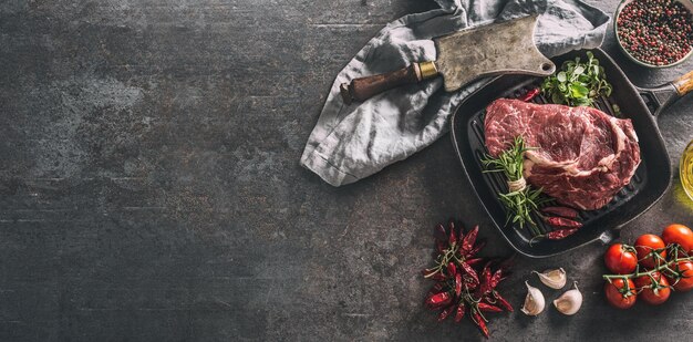 Beef ribe eye steak in grill pan with rosemary oregano salt pepper spices garlic and tomatoes