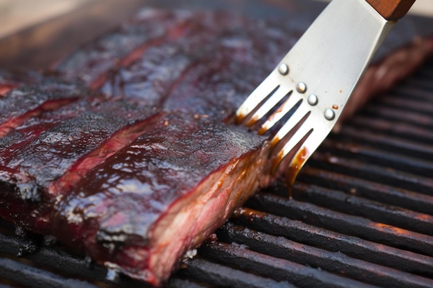 Beef ribs being basted with bbq sauce on a grill with a basting brush