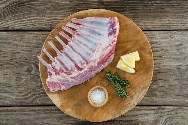 Beef ribs rack, rosemary herb, salt and lemon on wooden tray against wooden table