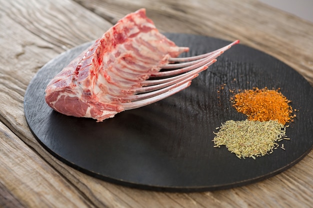 Beef ribs rack and spices on black round tray against wooden table