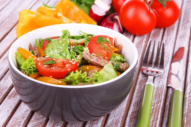 Beef salad in bowl with vegetables on wooden background