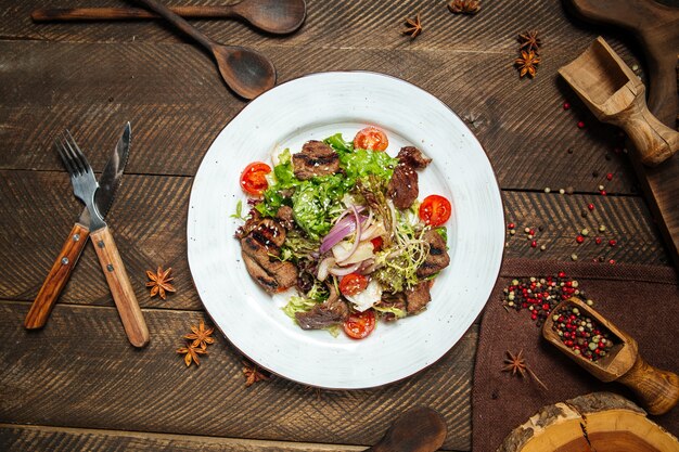 Beef salad with vegetables and greens on the wooden table