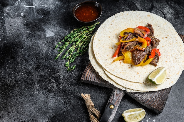 Beef Steak Fajitas with tortilla, mix pepper and onion traditional Mexican food. Black background. 