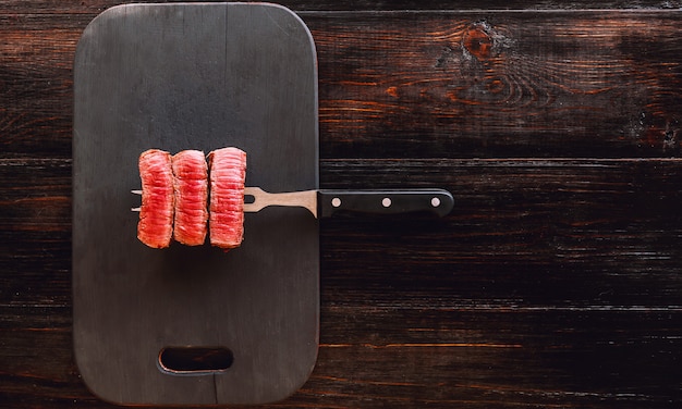 Beef steak on a fork on a dark wooden surface