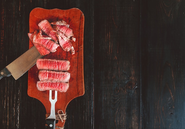 Beef steak on a fork on a dark wooden surface