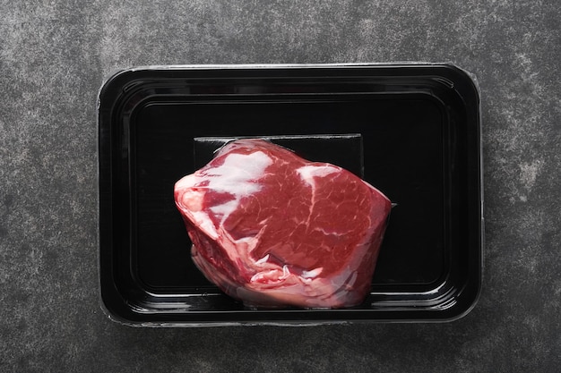 쇠고기 스테이크 검은 돌 배경에 진공 검정 플라스틱 팩에 포크와 로즈마리를 넣은 신선한 생 쇠고기 스테이크 Vacoom 패키지 디자인 아이디어를 위한 탑 뷰 모형