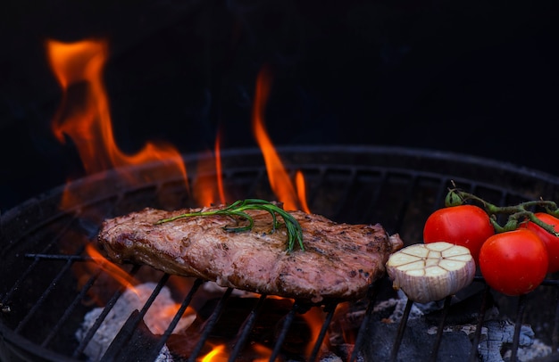 Beef steak on the grill grate, flames on background 