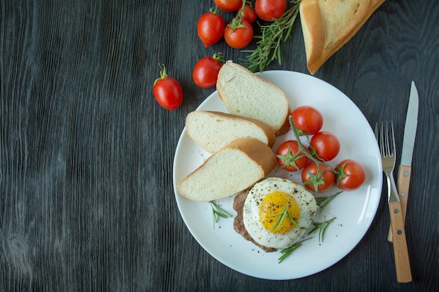 Beef steak with fried egg in spices served on a white plate. American dish. Dark wooden background. Side view. Close-up. Space for text.