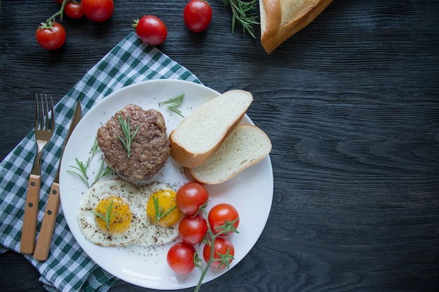 Beef steak with fried egg in spices served on a white plate. American dish. Dark wooden background. Side view. Close-up. Space for text.