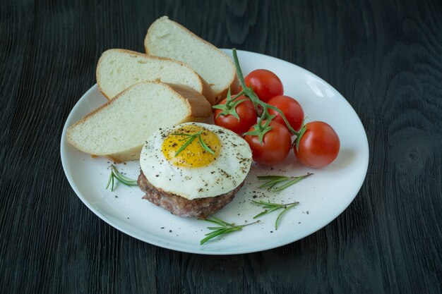 Beef steak with fried egg in spices served on a white plate. American dish. Dark wooden background. Side view. Close-up.