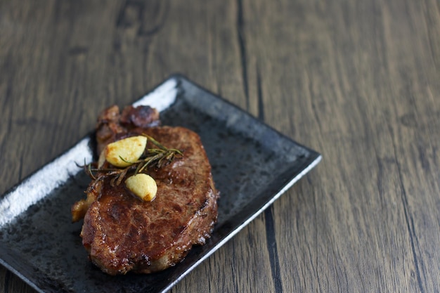 beef steak with garlic in black plate on wooden table