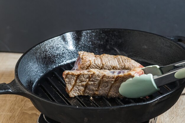 Beef steak with tongs on the grill pan