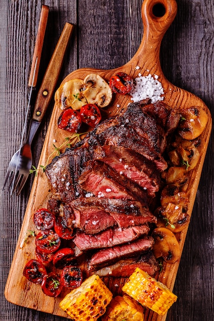 Beef steaks with grilled tomatoes, mushrooms and corn.