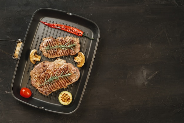 Beef steaks with vegetables on grill pan, top view