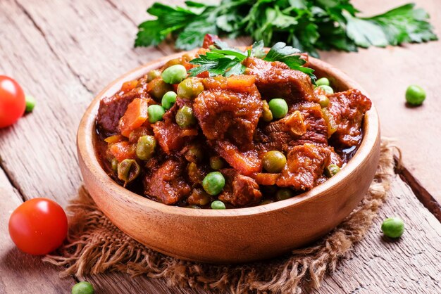 Stufato di manzo ragù di carne con carote cipolle e piselli vintage sfondo in legno fuoco selettivo