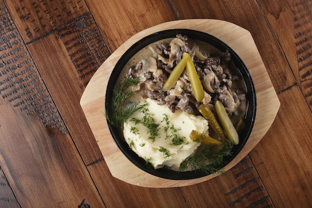 Beef stroganoff met aardappelpuree en ingelegde komkommers in een pan Houten achtergrond