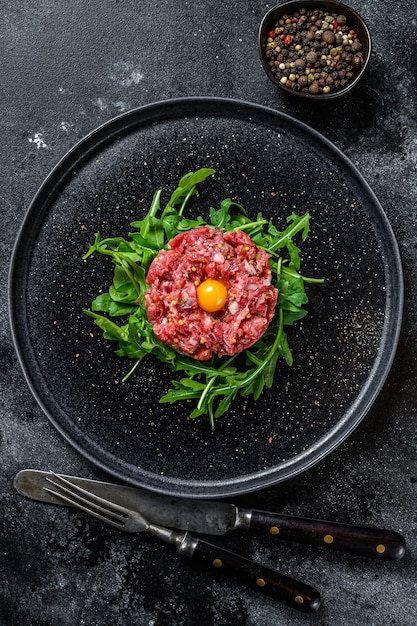 Photo beef tartar with a quail egg served on a black stone plate.. black background. top view.