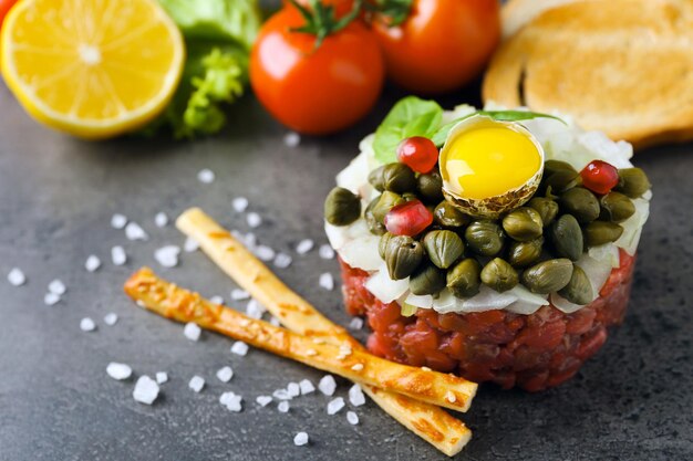 Beef tartare served with bread sticks on a grey surface close up