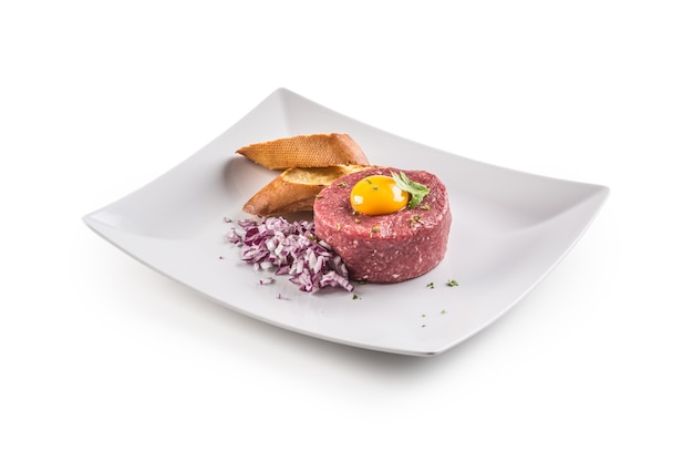 Beef tartare with egg yolk red onion herbs and bruschetta isolated on white.