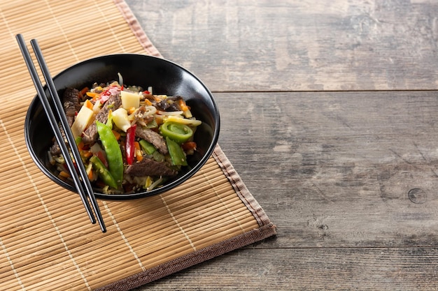 Beef, vegetables and sesame seeds in black bowl on wooden table