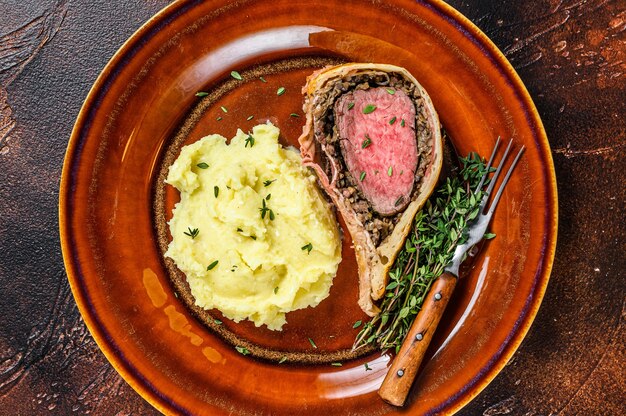 Beef Wellington-gebakje met gepureerde aardappel op een rustieke plaat.