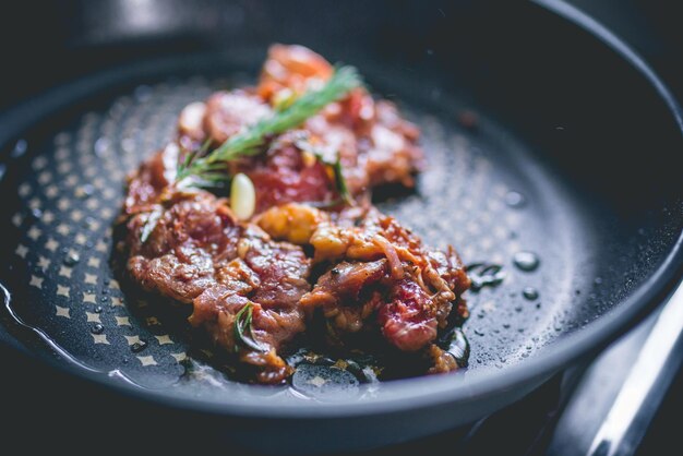 Beefsteak met rozemarijn, knoflook, zout en peper in een ijzeren pan.