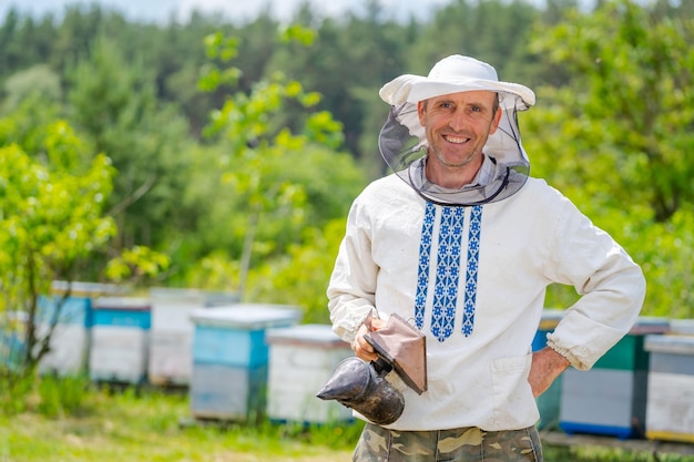 The beekeeper with a smoker in hands near a beehive