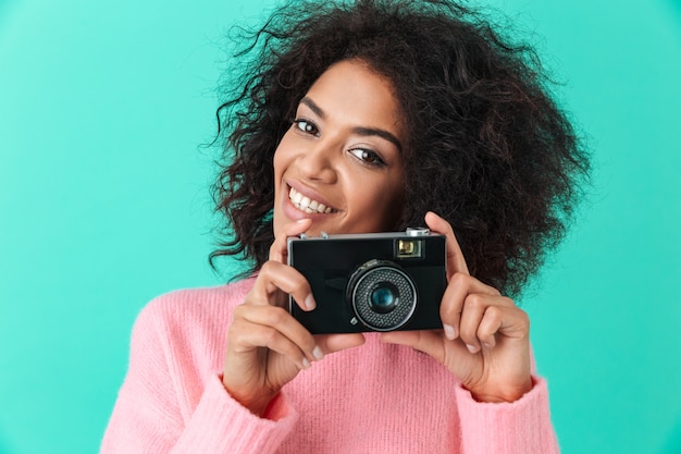 Beeld van blij volwassen meisje met retro camera in handen stellen, geïsoleerd tegen blauwe muur