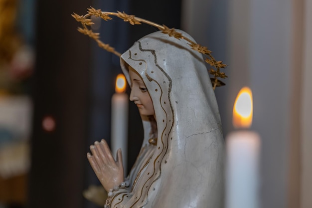 Beeld van de biddende Maagd Maria bij brandende kaarsen